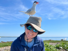 Lyra Brennan on beach wearing a bucket hat with a gull perched on top of her head